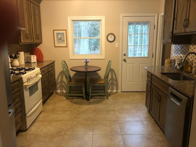 kitchen with decorative backsplash, stainless steel dishwasher, dark stone counters, gas range gas stove, and sink