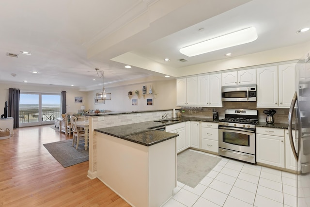 kitchen featuring decorative light fixtures, sink, white cabinets, kitchen peninsula, and stainless steel appliances