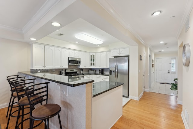 kitchen with appliances with stainless steel finishes, white cabinetry, a kitchen bar, ornamental molding, and kitchen peninsula