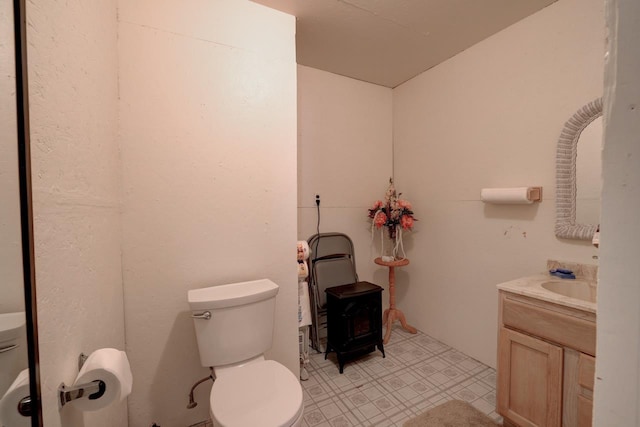 bathroom featuring toilet, a wood stove, tile patterned floors, and vanity