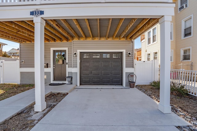 entrance to property featuring a garage, concrete driveway, and fence