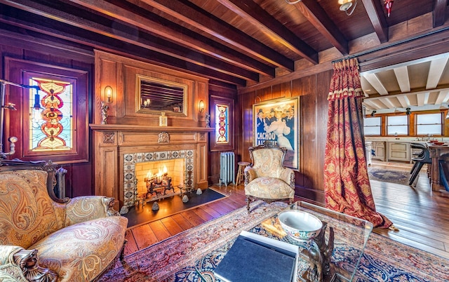 sitting room featuring beamed ceiling, hardwood / wood-style floors, a tile fireplace, and wood walls