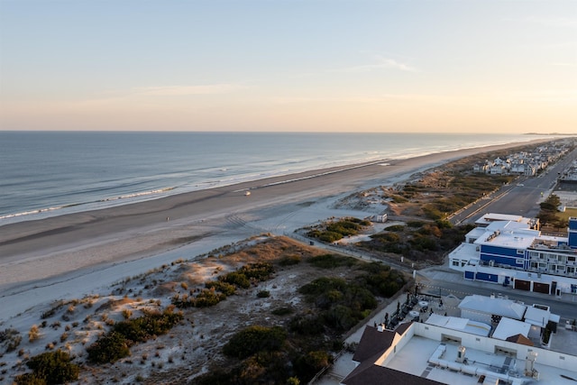 aerial view at dusk featuring a view of the beach and a water view