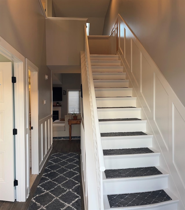 stairway with a fireplace, a high ceiling, and wood finished floors