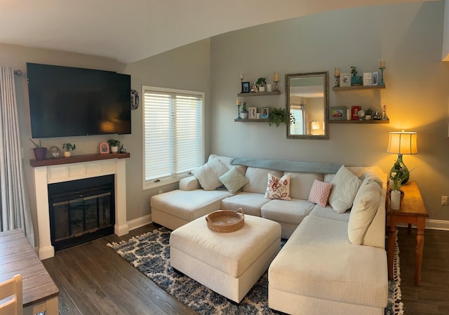 living room featuring baseboards, vaulted ceiling, dark wood-style flooring, and a glass covered fireplace