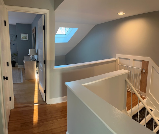 hallway with vaulted ceiling with skylight and hardwood / wood-style floors