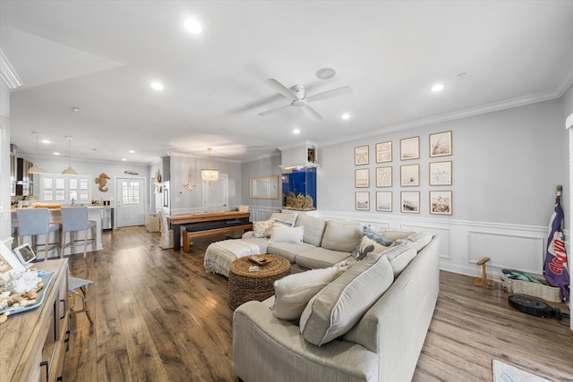 living room featuring wood finished floors, recessed lighting, wainscoting, crown molding, and ceiling fan