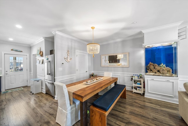 dining space with a wainscoted wall, ornamental molding, an inviting chandelier, and dark wood-style flooring