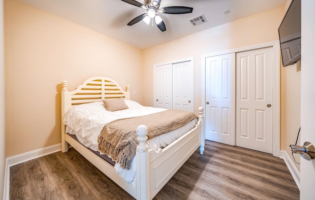 bedroom featuring multiple closets, baseboards, visible vents, and dark wood-type flooring