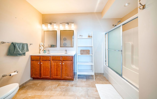 bathroom featuring double vanity, baseboards, toilet, combined bath / shower with glass door, and a sink