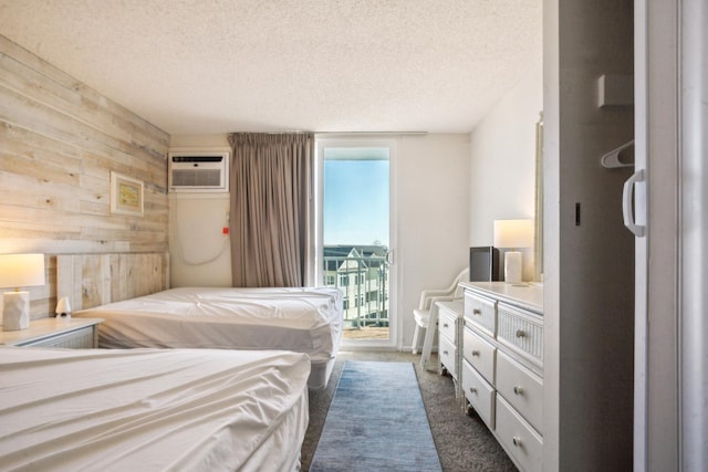 bedroom featuring access to exterior, wooden walls, a wall unit AC, a textured ceiling, and dark carpet