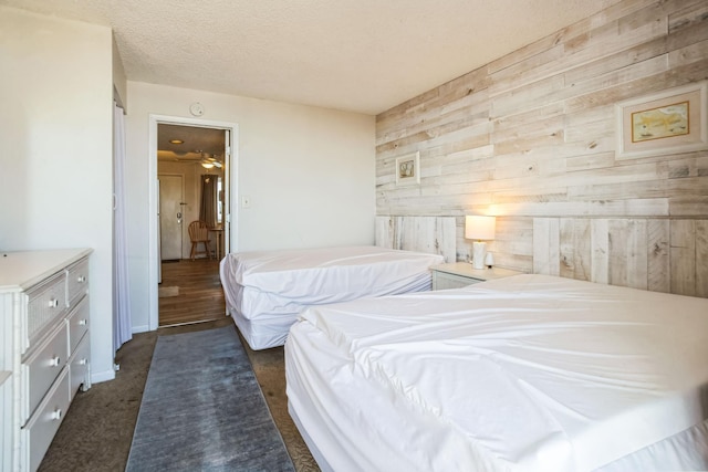 bedroom with wooden walls, a textured ceiling, and dark colored carpet