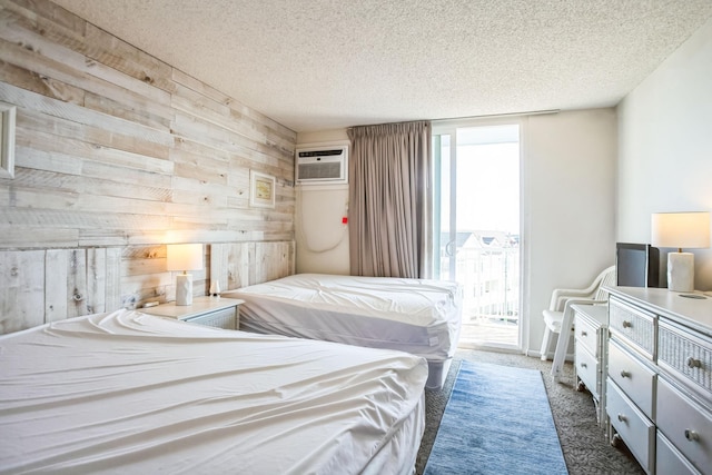 carpeted bedroom featuring access to outside, a wall unit AC, a textured ceiling, and wood walls