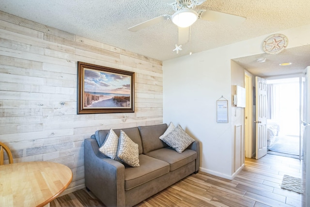 living room with ceiling fan, wood walls, a textured ceiling, and light wood-type flooring