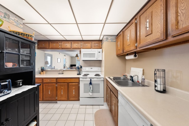 kitchen featuring a paneled ceiling, sink, light tile patterned floors, and white appliances