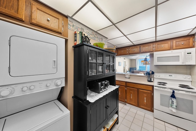 kitchen featuring a notable chandelier, stacked washer and dryer, white appliances, a paneled ceiling, and light tile patterned floors