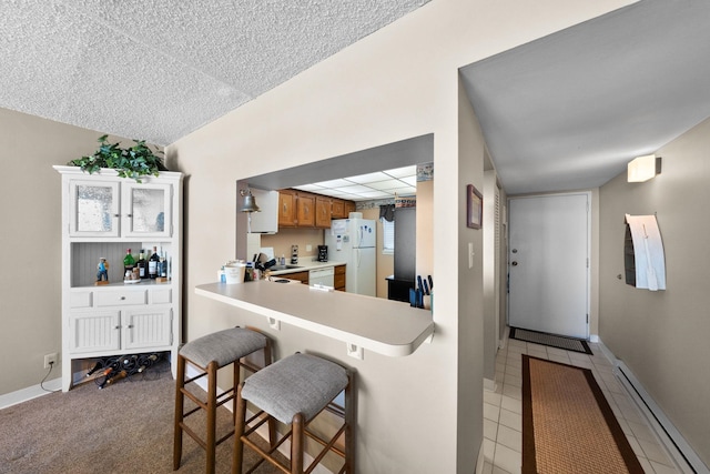 kitchen featuring white appliances, a baseboard heating unit, a kitchen breakfast bar, light tile patterned flooring, and kitchen peninsula