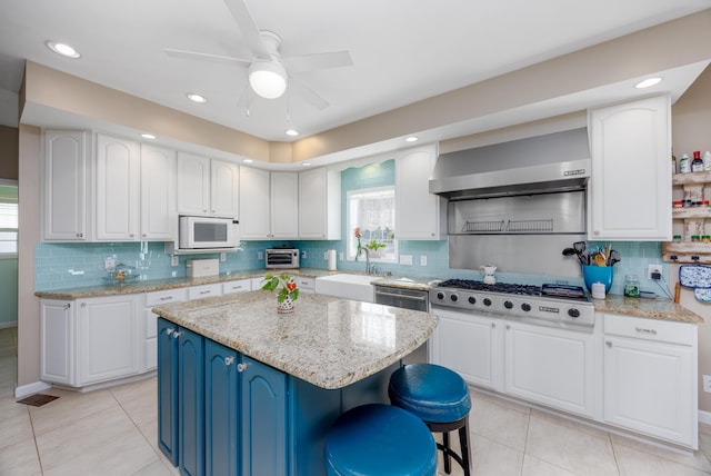 kitchen featuring blue cabinetry, white cabinetry, a center island, stainless steel appliances, and wall chimney range hood