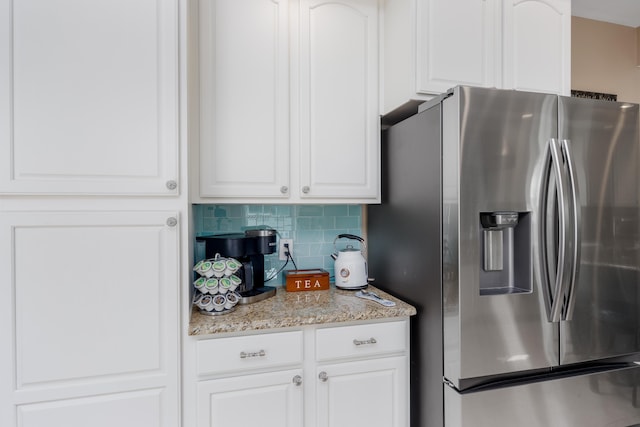 kitchen with backsplash, stainless steel fridge, white cabinetry, and light stone counters