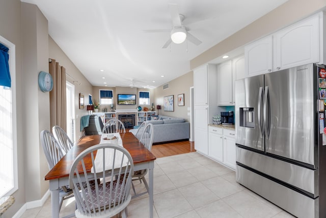 kitchen with stainless steel refrigerator with ice dispenser, light stone counters, ceiling fan, white cabinetry, and light tile patterned flooring