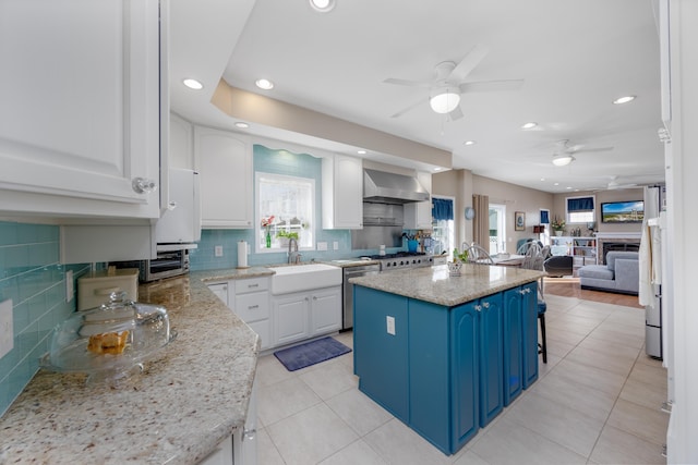 kitchen featuring wall chimney exhaust hood, sink, blue cabinetry, a center island, and white cabinetry