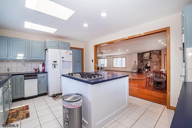 kitchen with decorative backsplash, a skylight, ceiling fan, white refrigerator with ice dispenser, and stainless steel gas stovetop