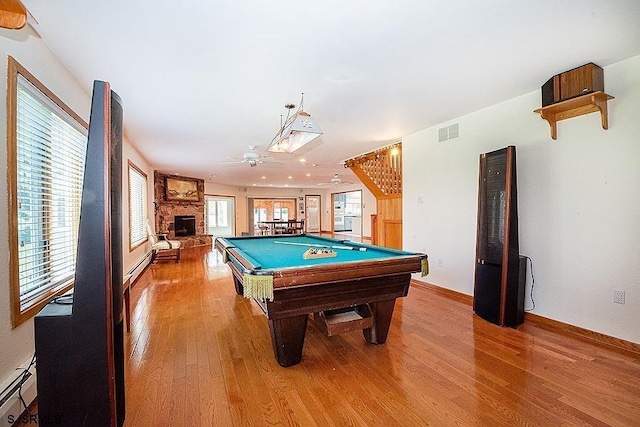 game room featuring ceiling fan, baseboard heating, a stone fireplace, hardwood / wood-style floors, and pool table