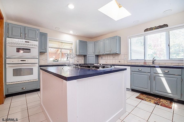 kitchen with a skylight, a center island, light tile patterned floors, and white appliances