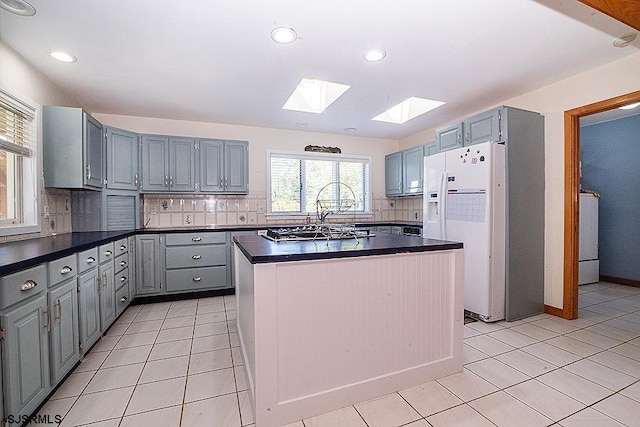 kitchen with decorative backsplash, light tile patterned flooring, white refrigerator with ice dispenser, and a skylight