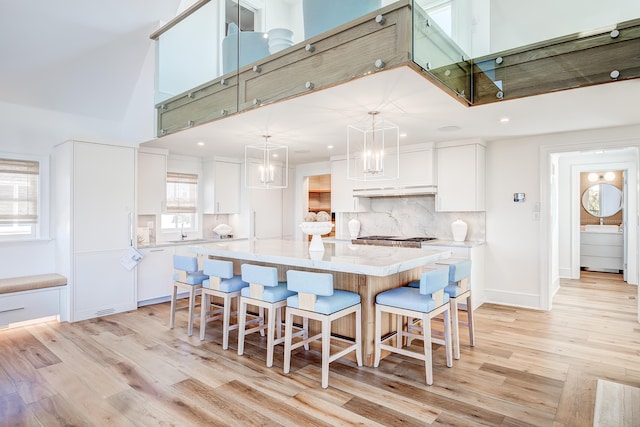 kitchen featuring decorative backsplash, light stone counters, a kitchen island, decorative light fixtures, and white cabinetry