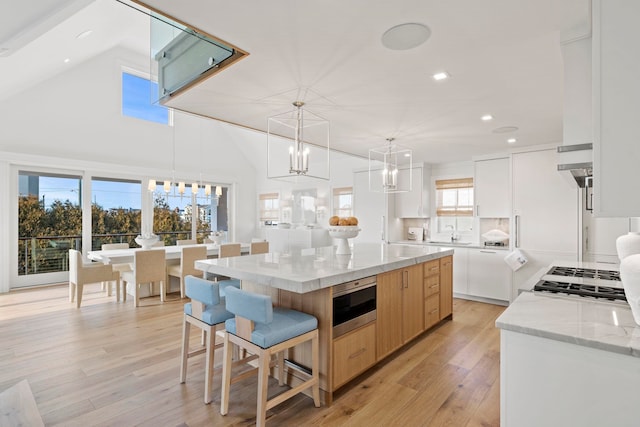 kitchen with pendant lighting, white cabinets, light hardwood / wood-style flooring, light stone countertops, and a large island