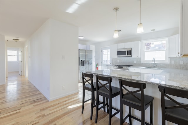 kitchen with white cabinets, decorative backsplash, light stone countertops, a kitchen bar, and stainless steel appliances