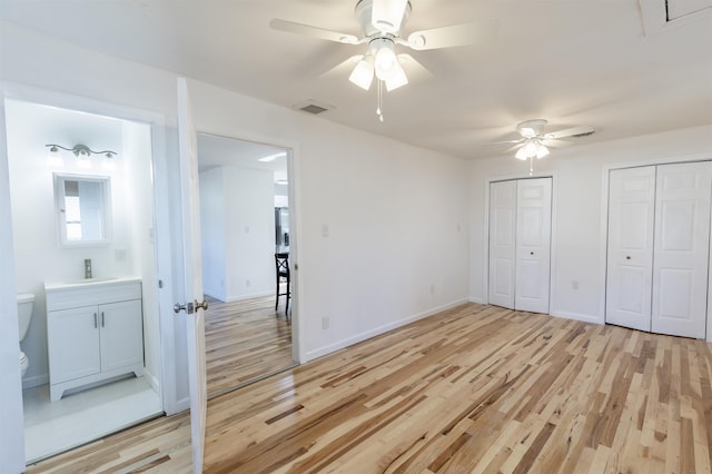 unfurnished bedroom with ceiling fan, sink, connected bathroom, light hardwood / wood-style floors, and multiple closets