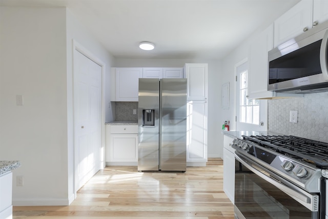 kitchen featuring white cabinets, stainless steel appliances, light stone countertops, and light hardwood / wood-style floors