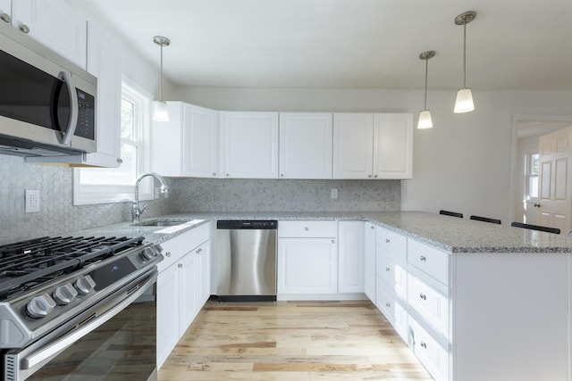 kitchen featuring white cabinetry, sink, kitchen peninsula, decorative light fixtures, and appliances with stainless steel finishes