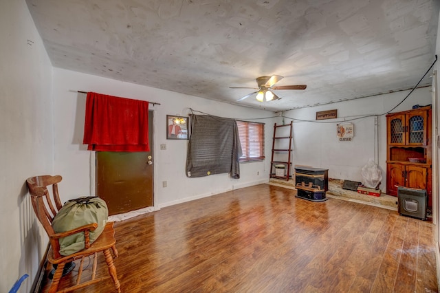 sitting room with wood-type flooring, ceiling fan, and a wood stove