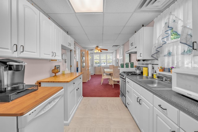 kitchen with white cabinetry, a drop ceiling, ceiling fan, sink, and stainless steel gas range oven