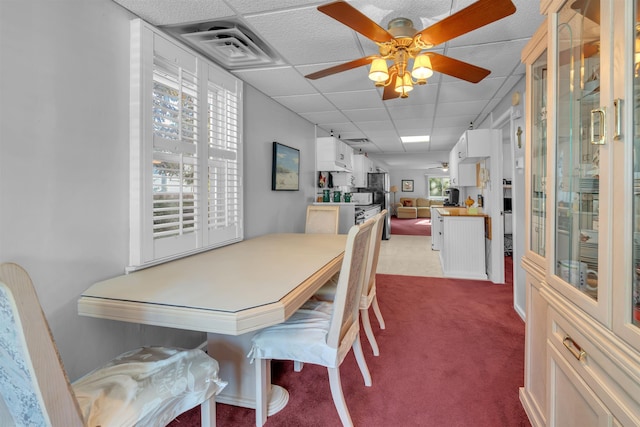 carpeted dining space featuring ceiling fan and a drop ceiling