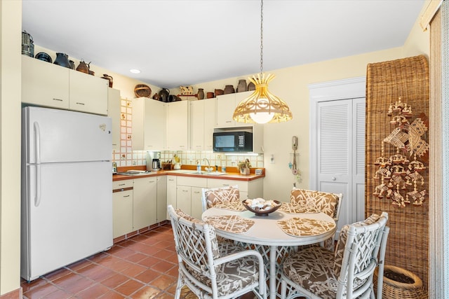 kitchen with pendant lighting, dark tile patterned flooring, white refrigerator, sink, and decorative backsplash