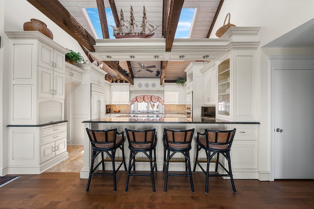 kitchen with a kitchen breakfast bar, dark wood-type flooring, white cabinets, and wooden ceiling