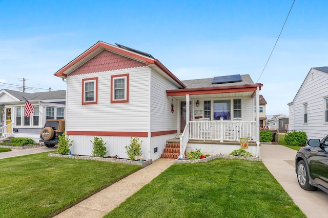 view of front of home featuring covered porch, roof mounted solar panels, and a front yard