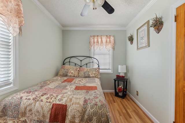 bedroom with light wood-type flooring, a textured ceiling, crown molding, a ceiling fan, and baseboards
