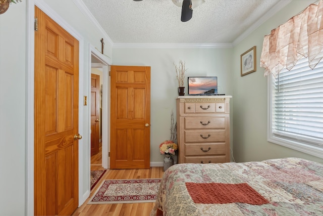 bedroom with light wood-style floors, a textured ceiling, ornamental molding, and a ceiling fan