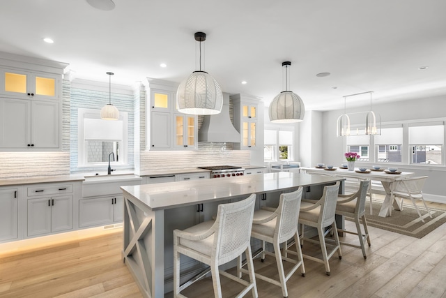207 120th St, Stone Harbor, NJ 08247 - kitchen with custom range hood, decorative backsplash, a kitchen island, light wood-style flooring, and a breakfast bar area