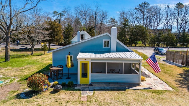 view of front of property with a chimney, a front yard, a sunroom, metal roof, and fence