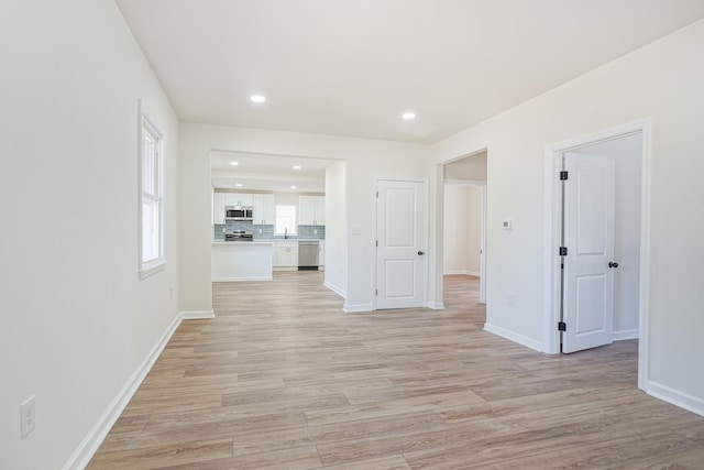 spare room featuring baseboards, a sink, light wood-style flooring, and recessed lighting