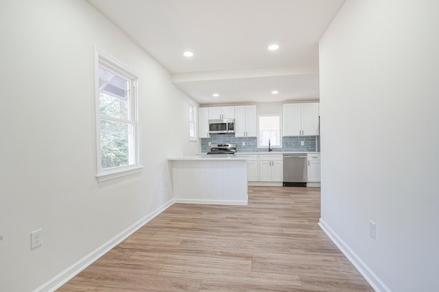 kitchen featuring light wood-style flooring, baseboards, white cabinets, appliances with stainless steel finishes, and tasteful backsplash