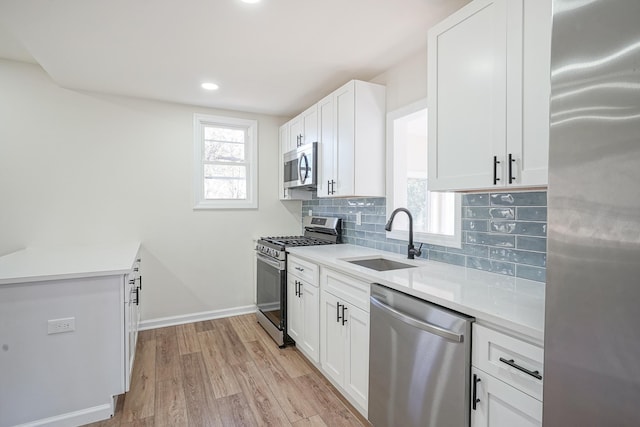 kitchen with appliances with stainless steel finishes, backsplash, a sink, light wood-style floors, and a wealth of natural light