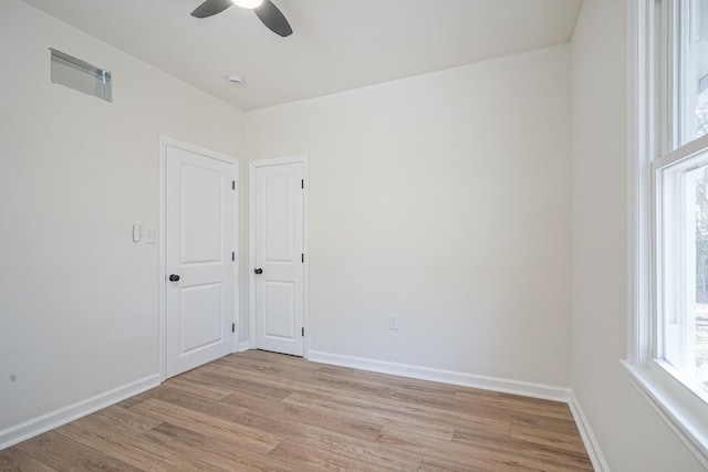 empty room with light wood finished floors, a ceiling fan, and baseboards