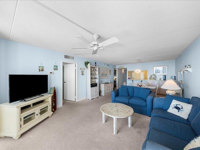 living room with a textured ceiling, ceiling fan, and light colored carpet